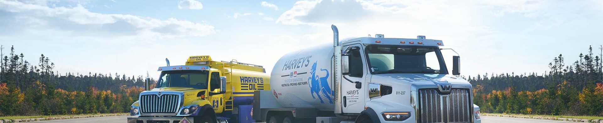 Two Harvey's fuel trucks, positioned in a vacant lot with a bright summer sky overhead.