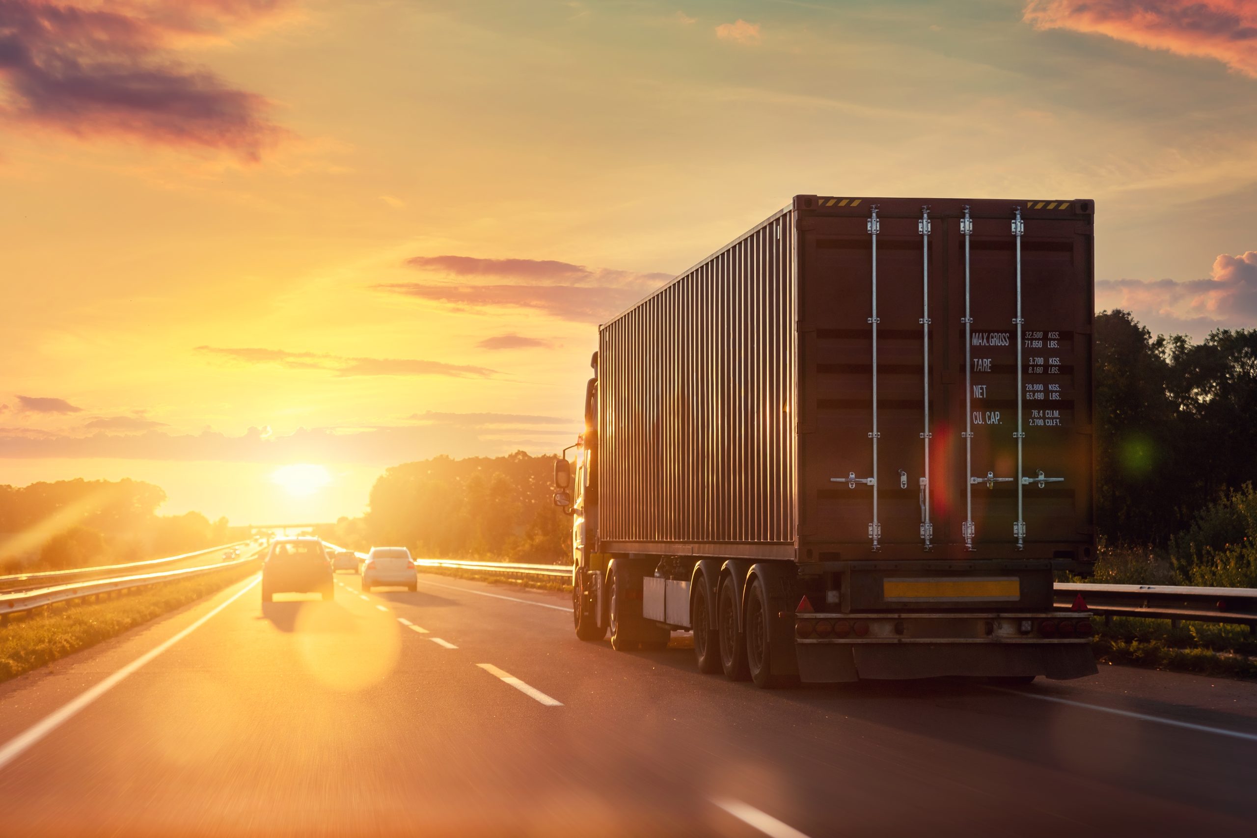 A diesel transport truck driving on the highway towards a sunset.