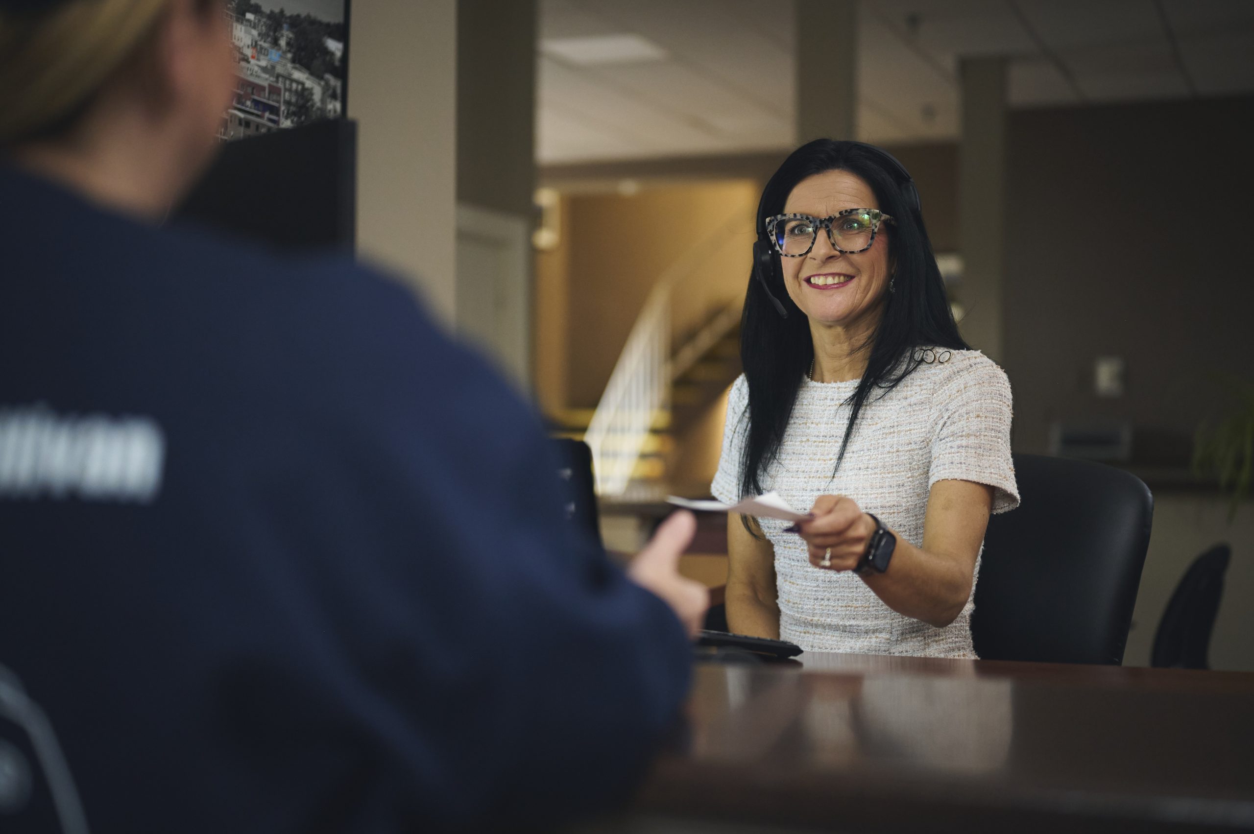 Harvey's receptionist sitting at the front desk, passing a customer a sheet of paper with a friendly smile.