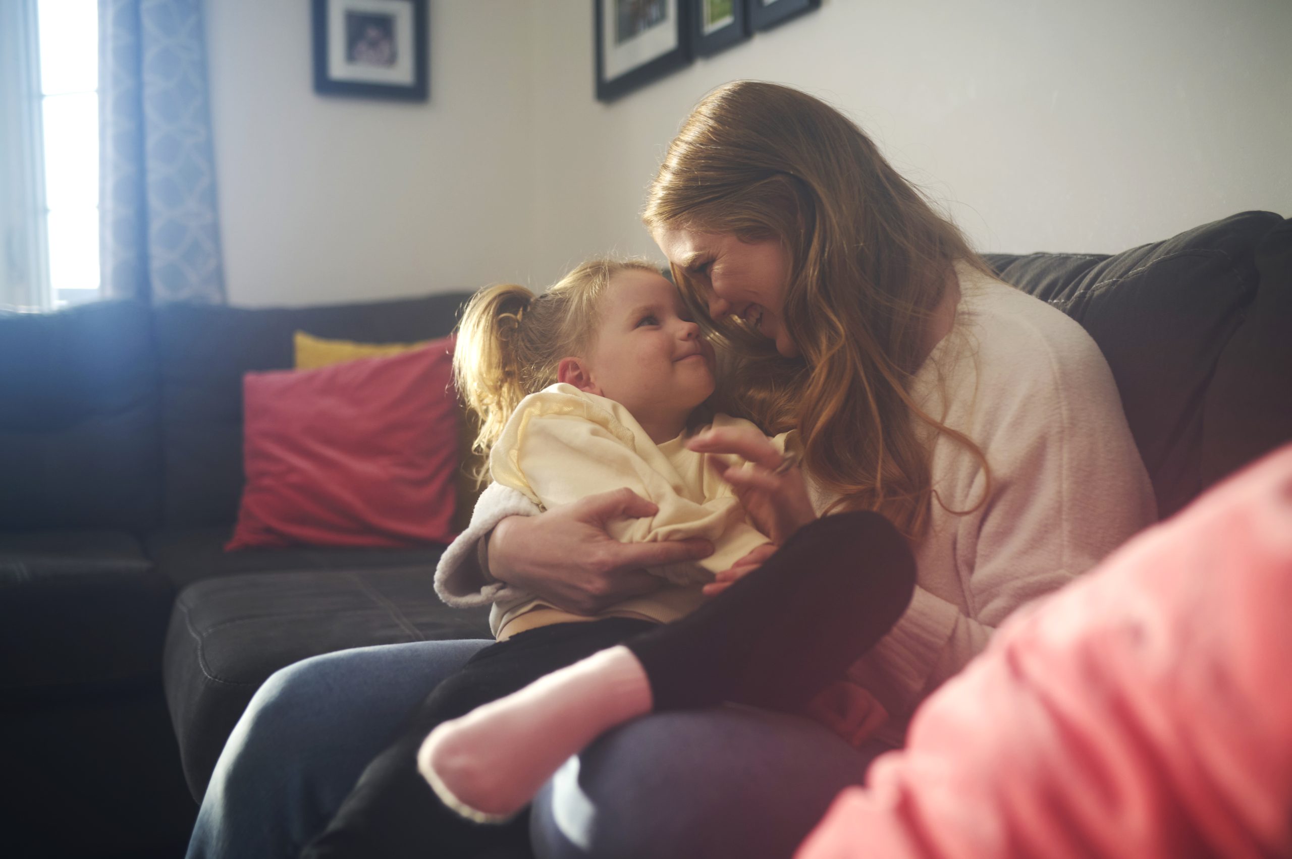 A mother and her young daughter snuggling and laughing on their living room couch.