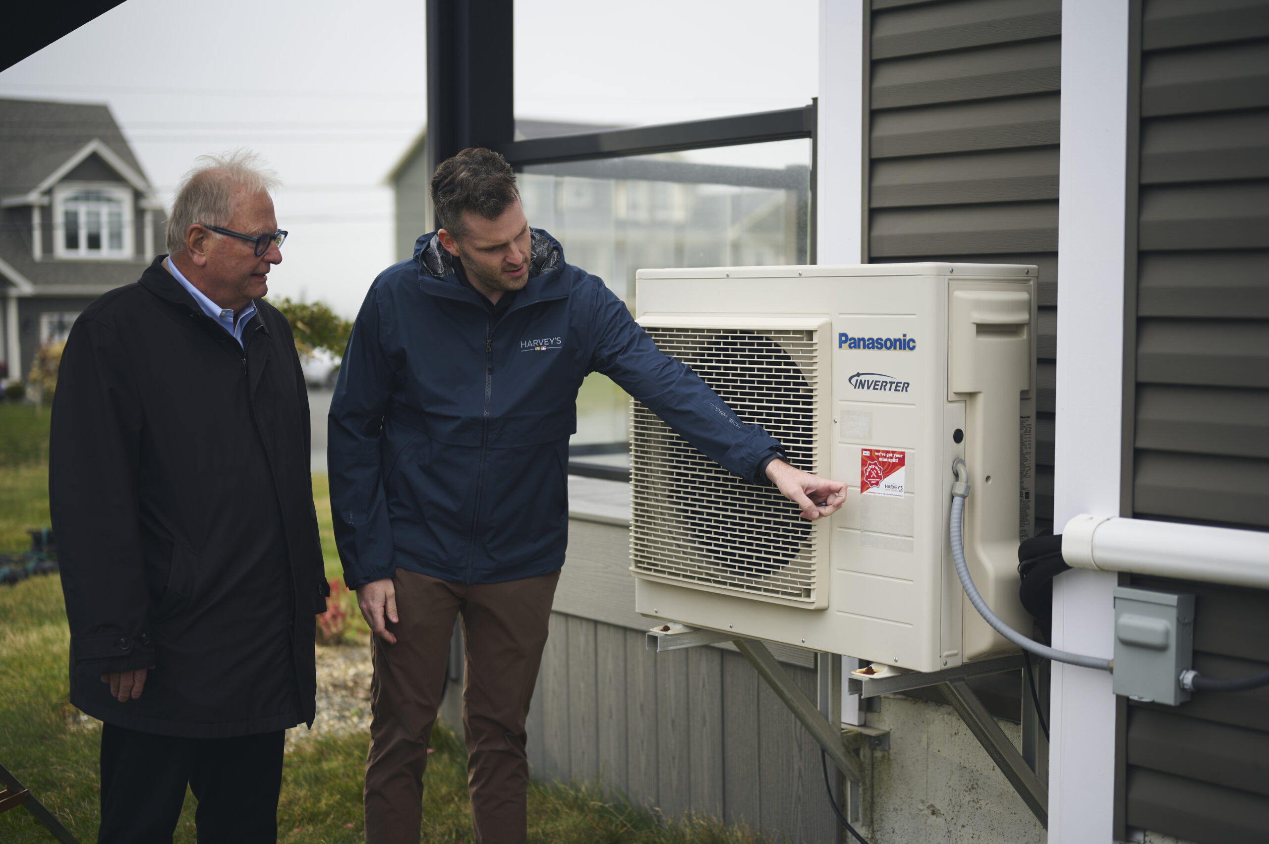 A Harvey's employee showing a customer their new outdoor heat pump unit, attached to their residential home.