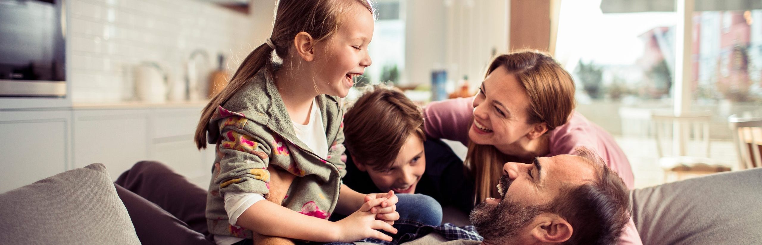 A family of four in their residential home, laughing together on their couch.