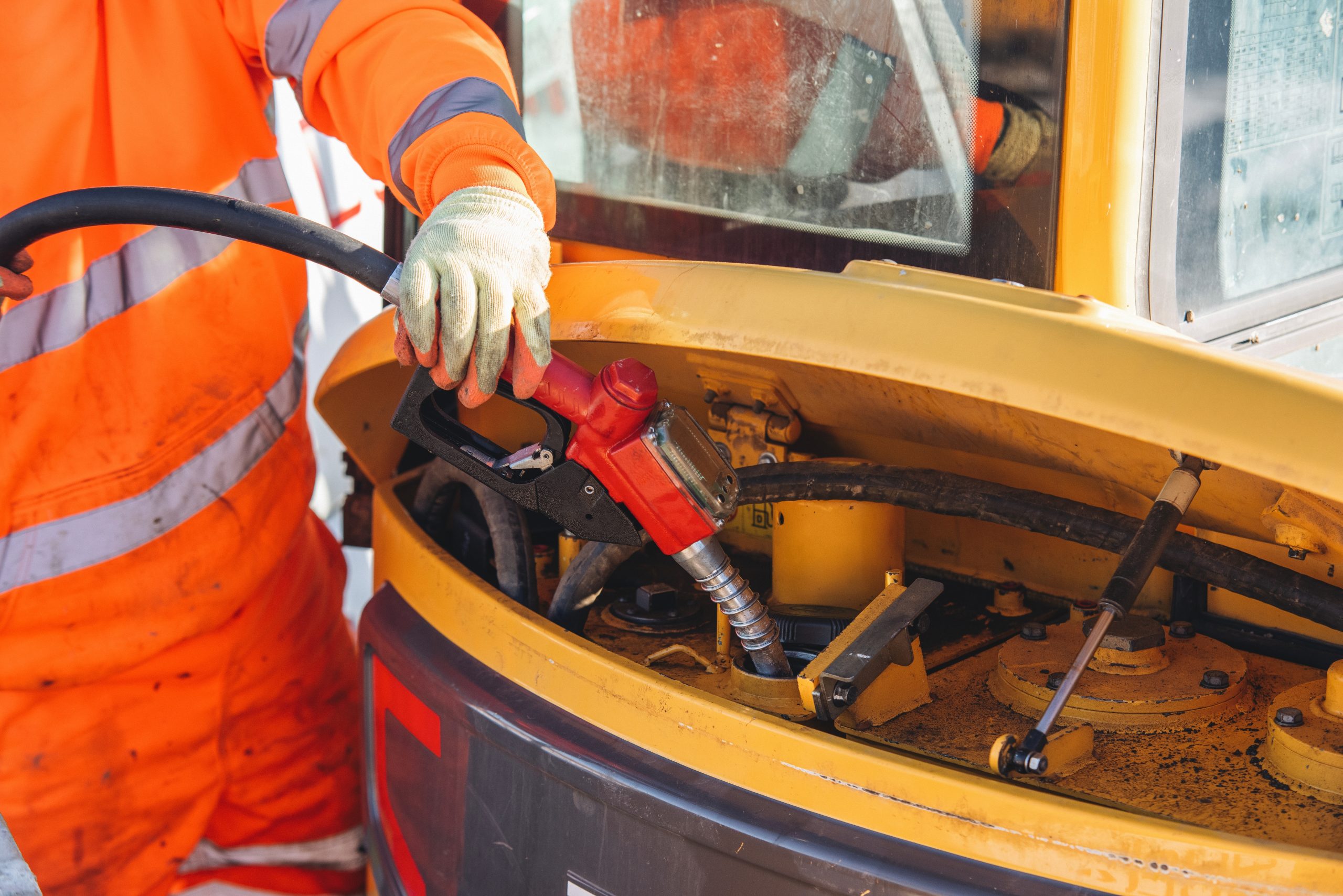 A mechanic in a bright orange uniform refuels heavy machinery at a construction site.