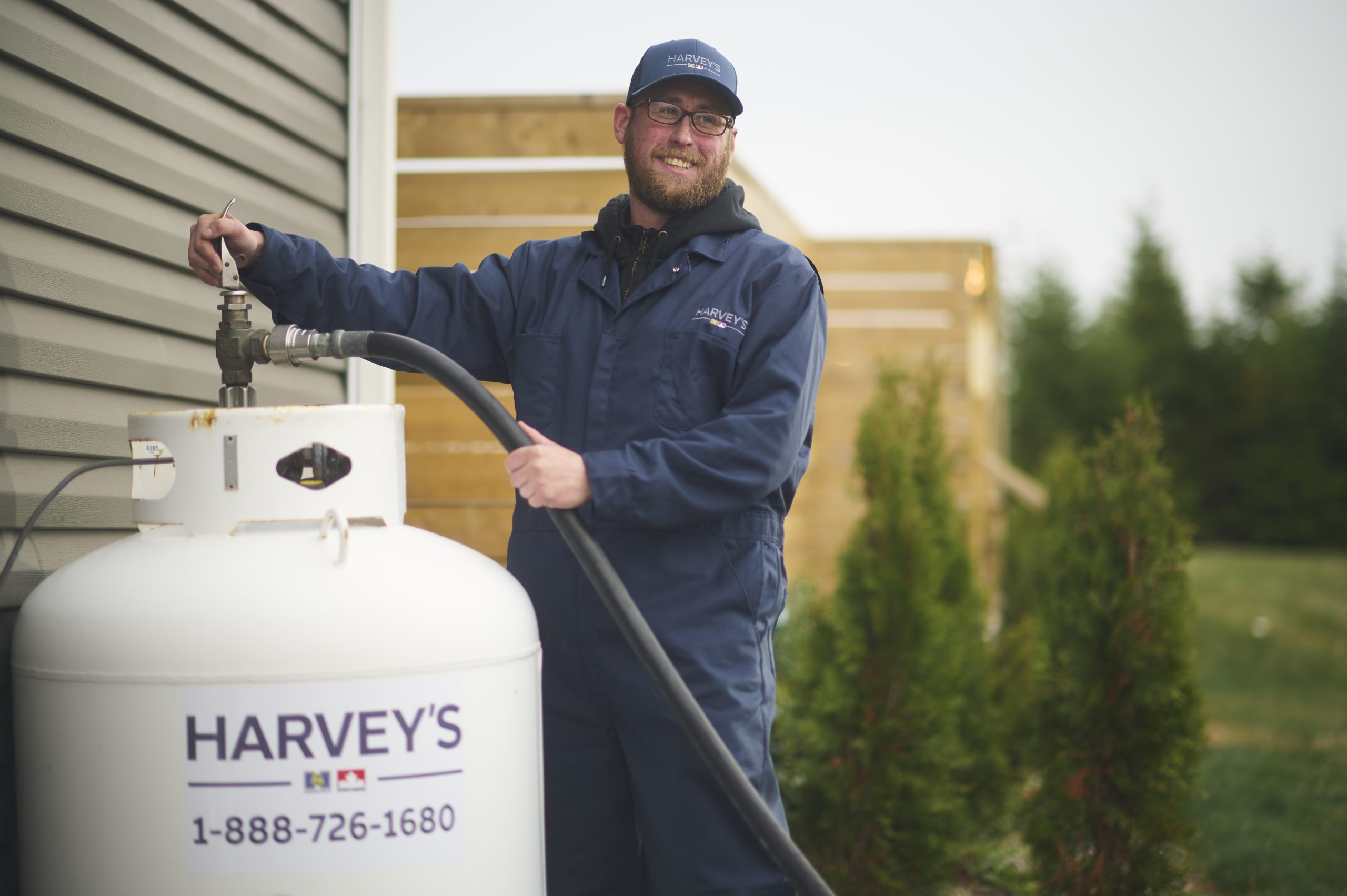 A friendly Harvey's employee refilling a propane tank attached to a residential home.